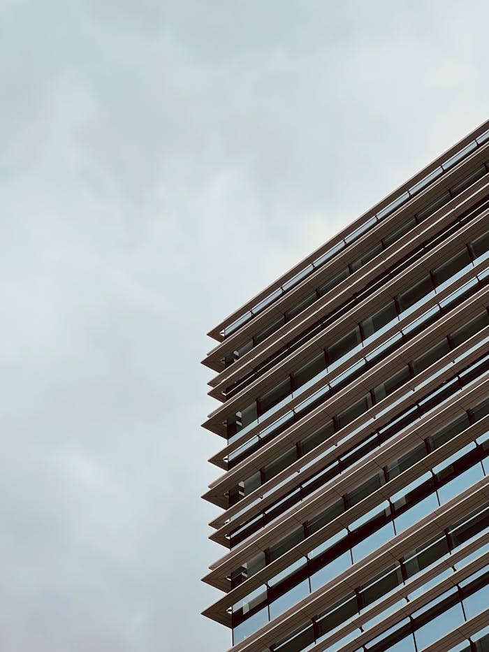 Low angle view of modern glass skyscraper with cloudy sky background.